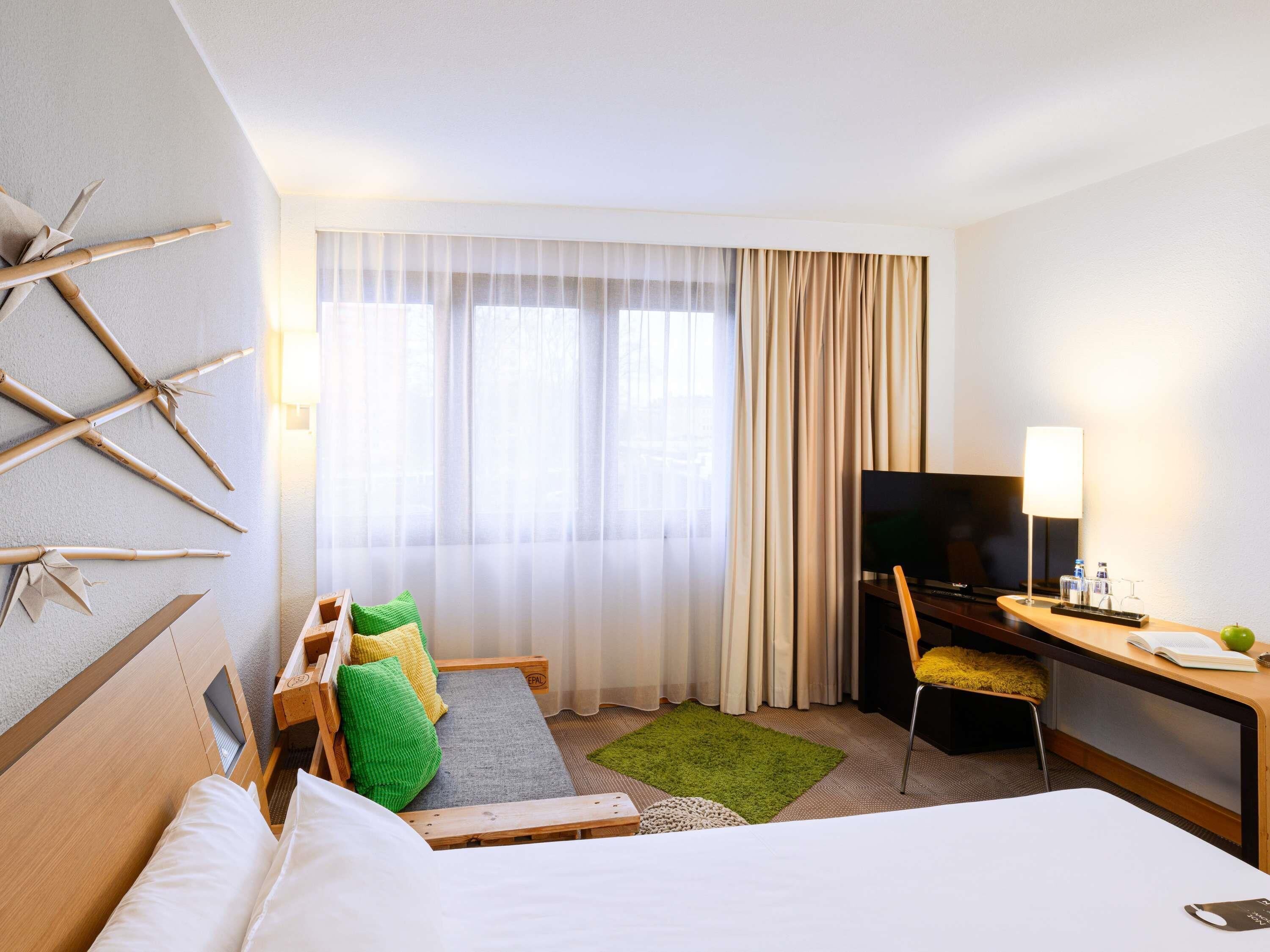 Habitación de hotel con cama, escritorio con televisor, silla y ventana con cortinas.