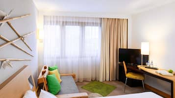 Habitación de hotel con cama, escritorio con televisor, silla y ventana con cortinas.