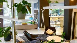 A modern interior with a seating area, a large potted plant, and a view of the dining area. - Novotel Gdansk Centrum (Gdansk)