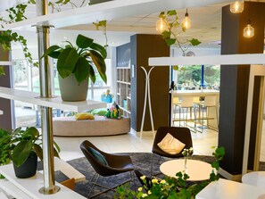 A modern interior with a seating area, a large potted plant, and a view of the dining area. - Novotel Gdansk Centrum (Gdansk)