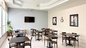 A modern dining area with multiple tables and chairs, a flat-screen TV mounted on the wall, and a clock. - Quality Inn & Suites Greenville I-65 (Greenville)