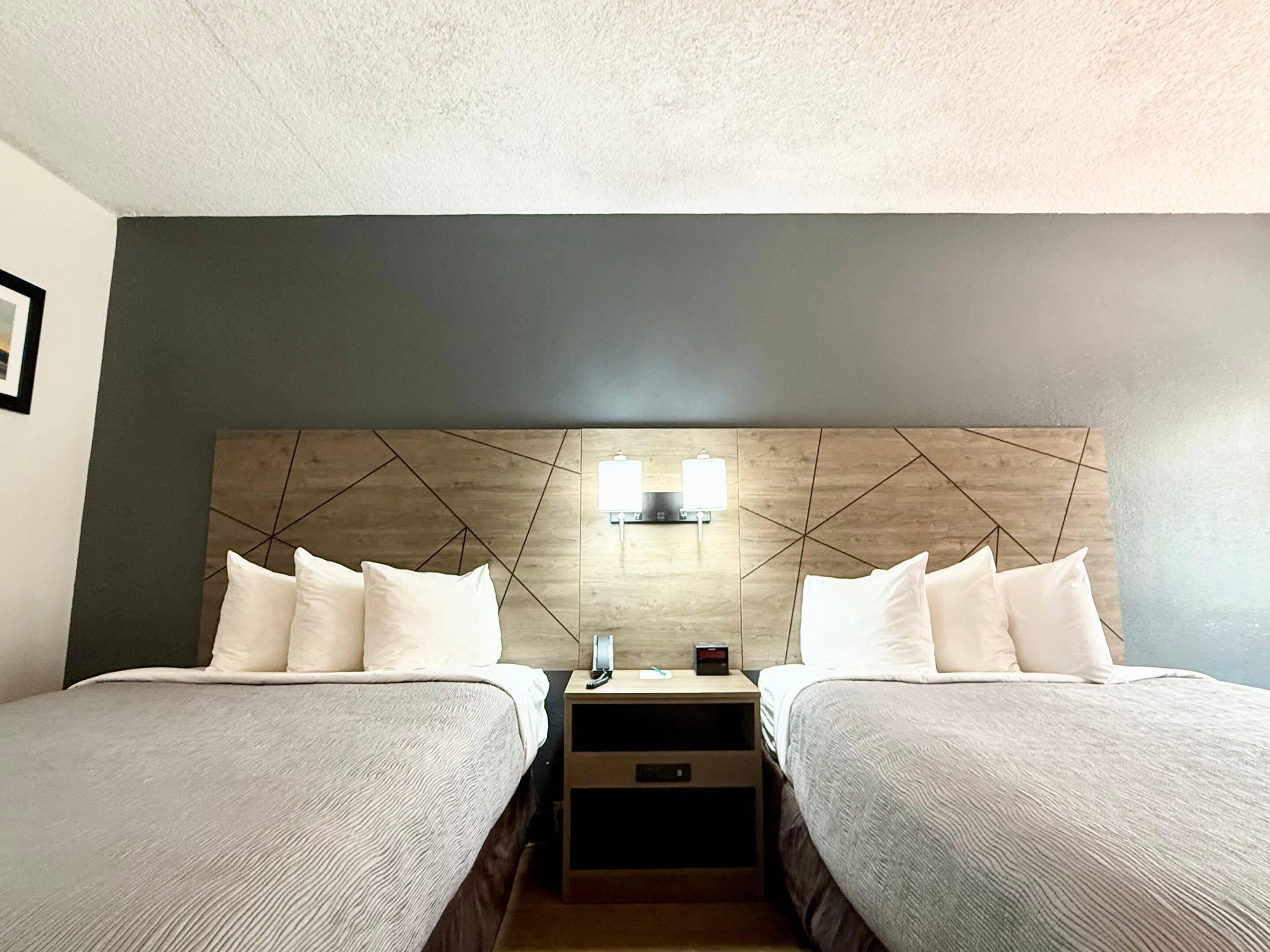 Una habitación de hotel con dos camas, cabecero de madera, mesitas de noche y una lámpara de pared.