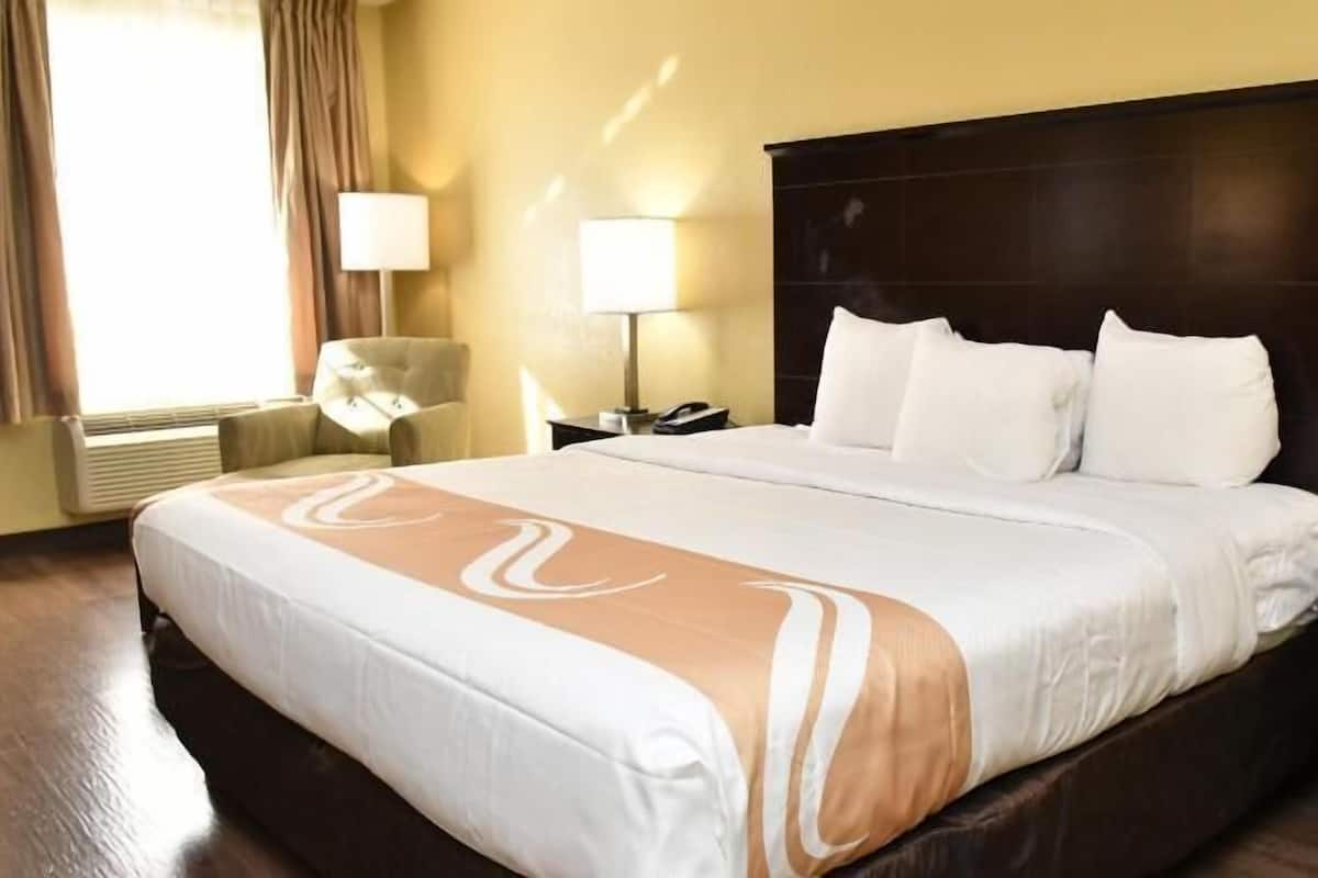 A hotel room with a large bed, a chair, a nightstand, and a lamp.