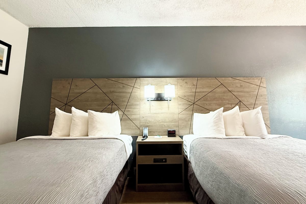 A hotel room with two beds, a wooden headboard, bedside tables, and a nightstand.