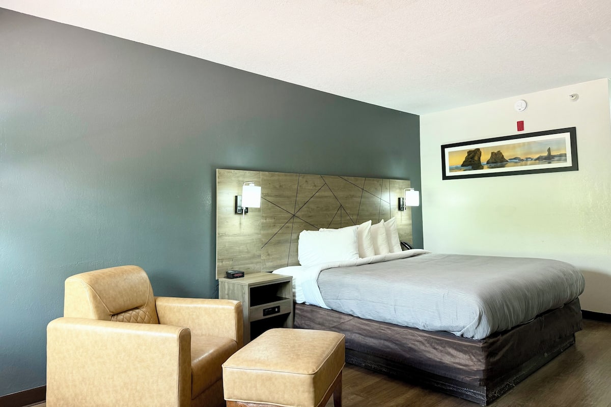 A hotel room with a bed, a chair, a nightstand, and a wall-mounted picture.