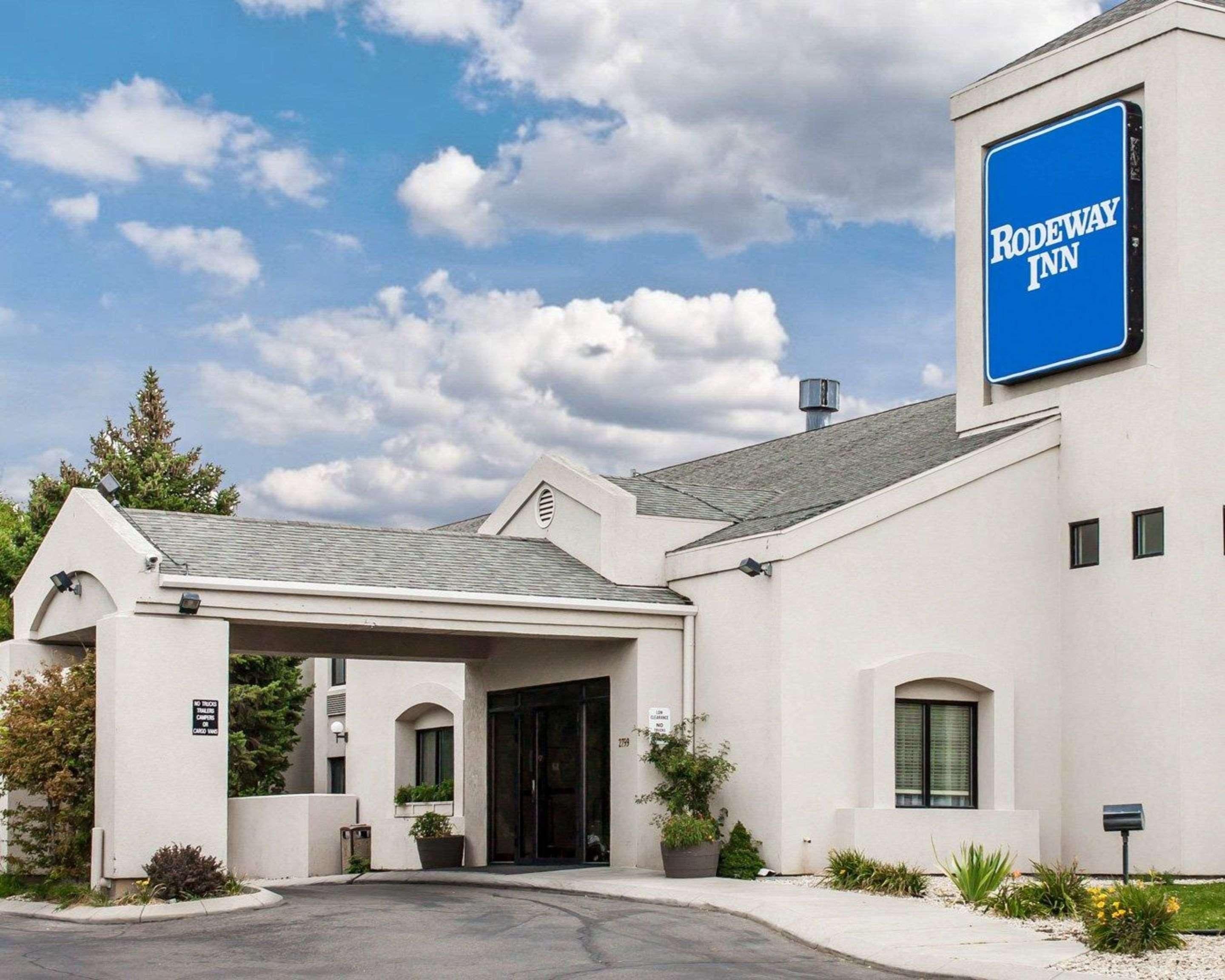 Un hôtel Rodeway Inn au style architectural moderne, caractérisé par une enseigne bleue bien visible, une entrée abritée et un jardin paysager à l’avant.
