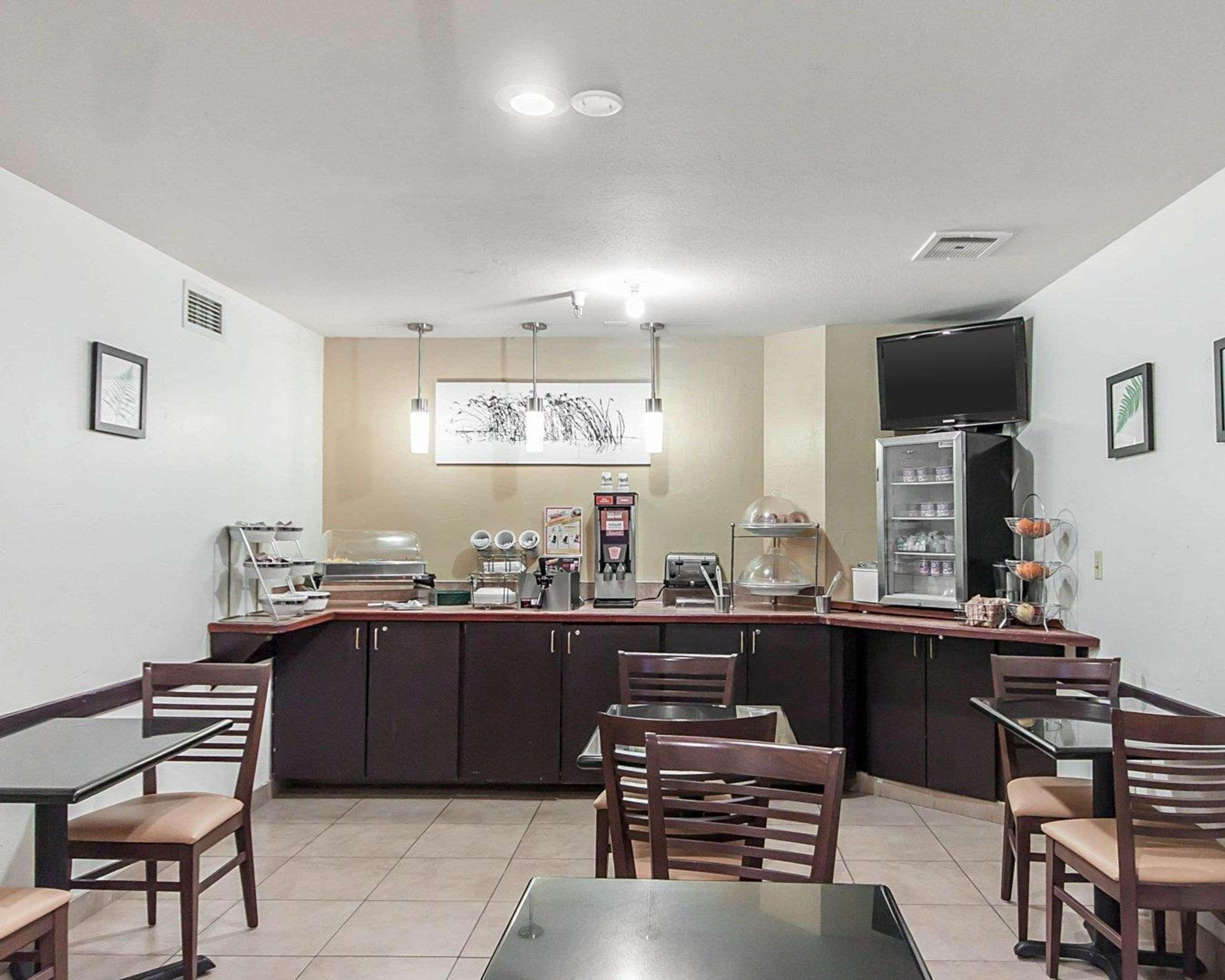 A restaurant with a counter, chairs, tables, a coffee machine, a refrigerator, and a TV mounted on the wall.
