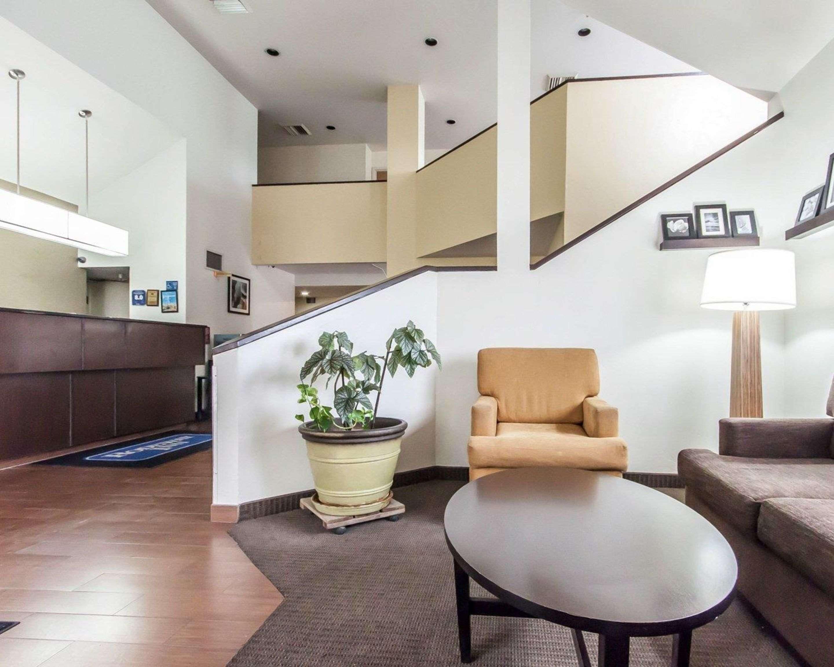 A modern lobby with a reception desk, a staircase, a potted plant, and seating areas.