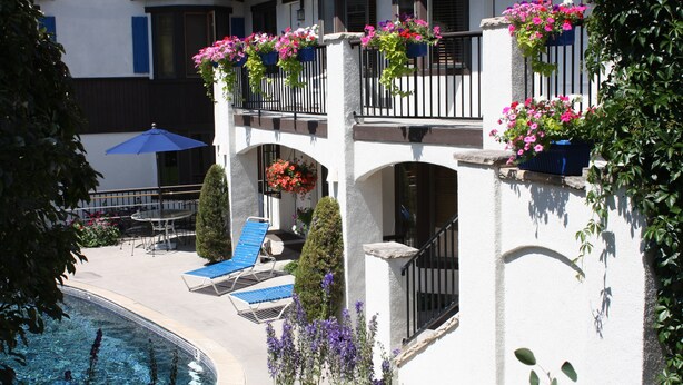 Un hotel con piscina, mobiliario exterior y jardineras en los balcones.