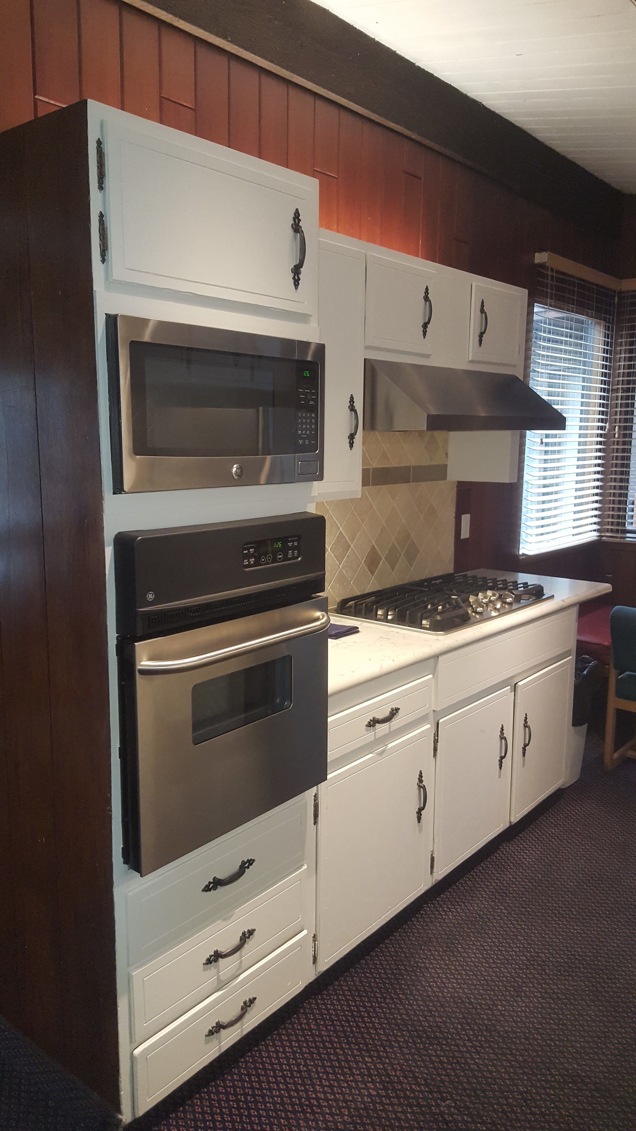 A kitchen with white cabinets, a microwave, an oven, a stove, and a range hood.