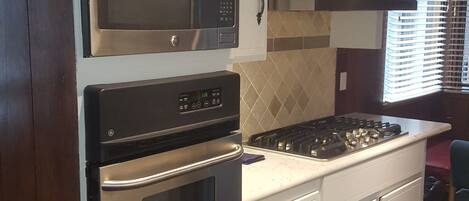 A kitchen with white cabinets, a microwave, an oven, a stove, and a range hood.