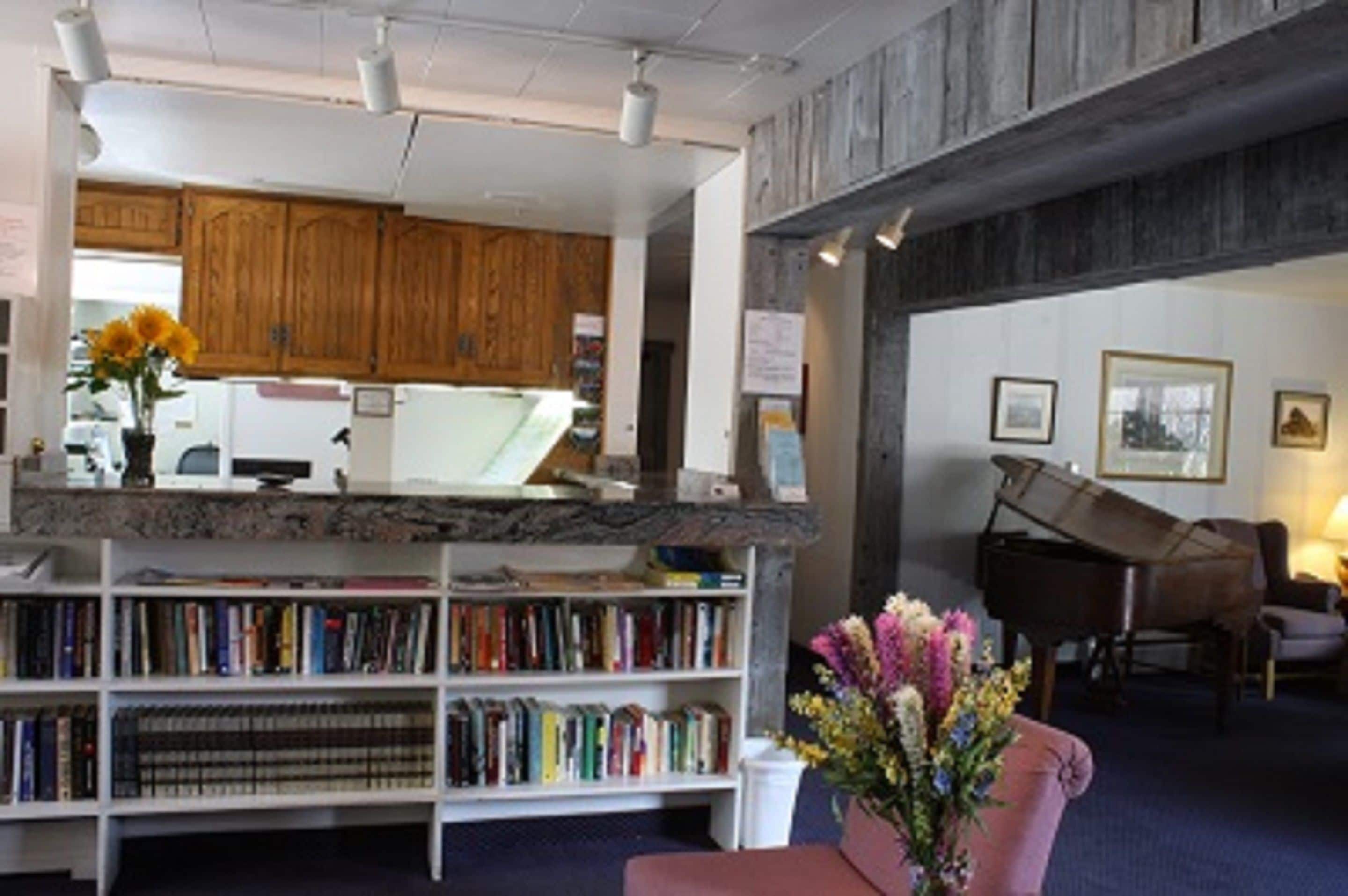 A library with bookshelves, a piano, and a vase of flowers.