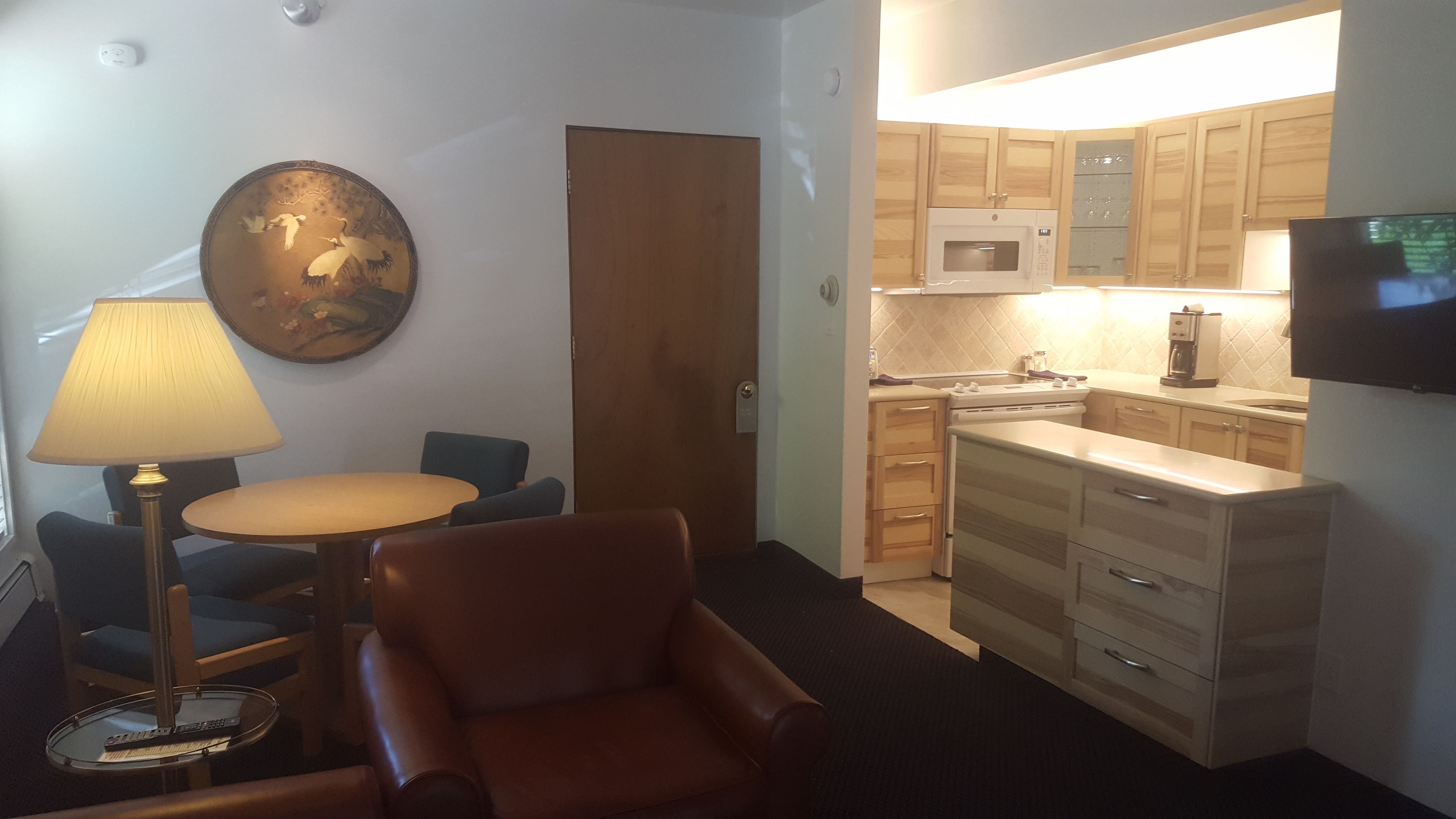 A compact living space with a kitchenette, a dining area with a table and chairs, and a seating area with a chair and a lamp.