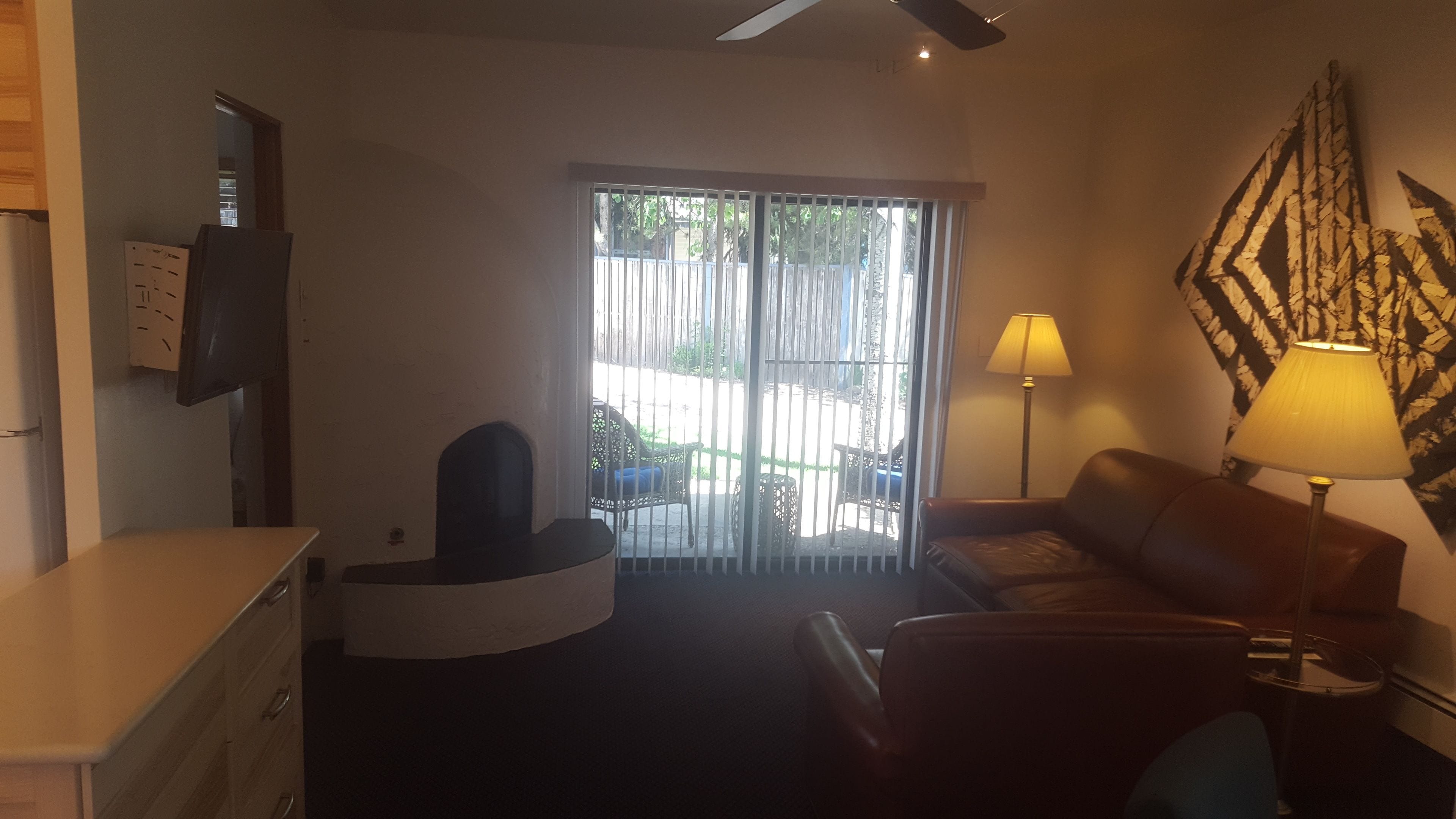 A living room with a sofa, a coffee table, a TV mounted on the wall, and a sliding glass door leading to an outdoor area.
