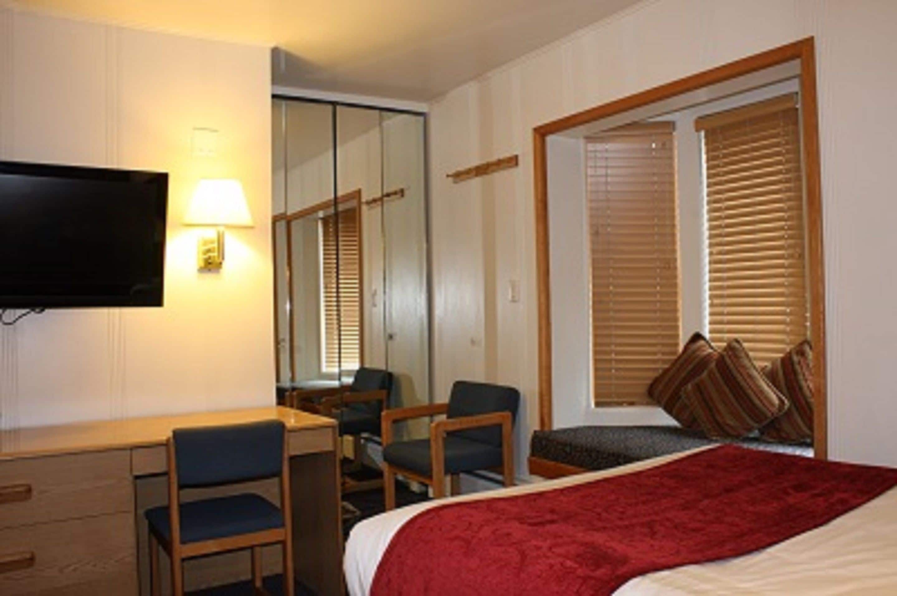 A hotel room with a bed, a desk, two chairs, a television, and a window with blinds.