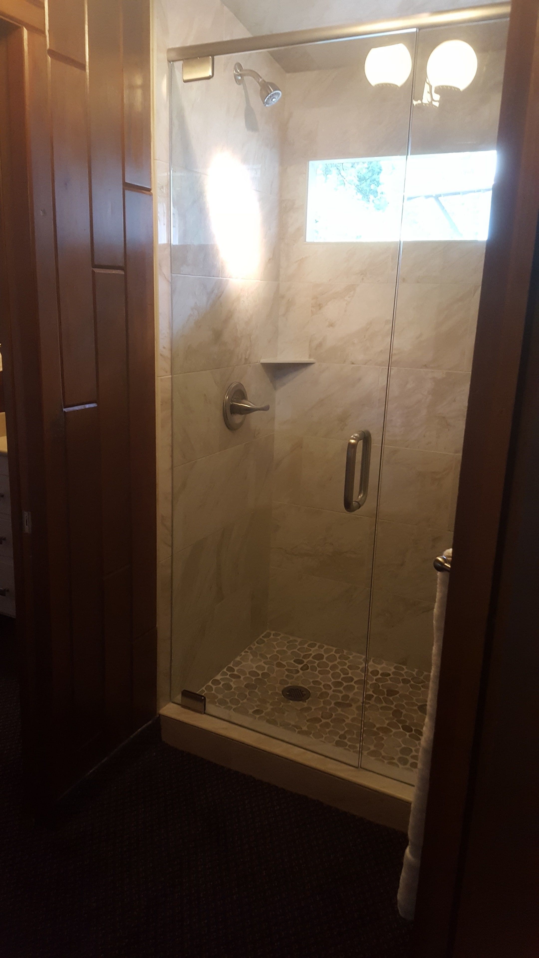 A glass-enclosed shower with a handheld showerhead, a small shelf, and a window.