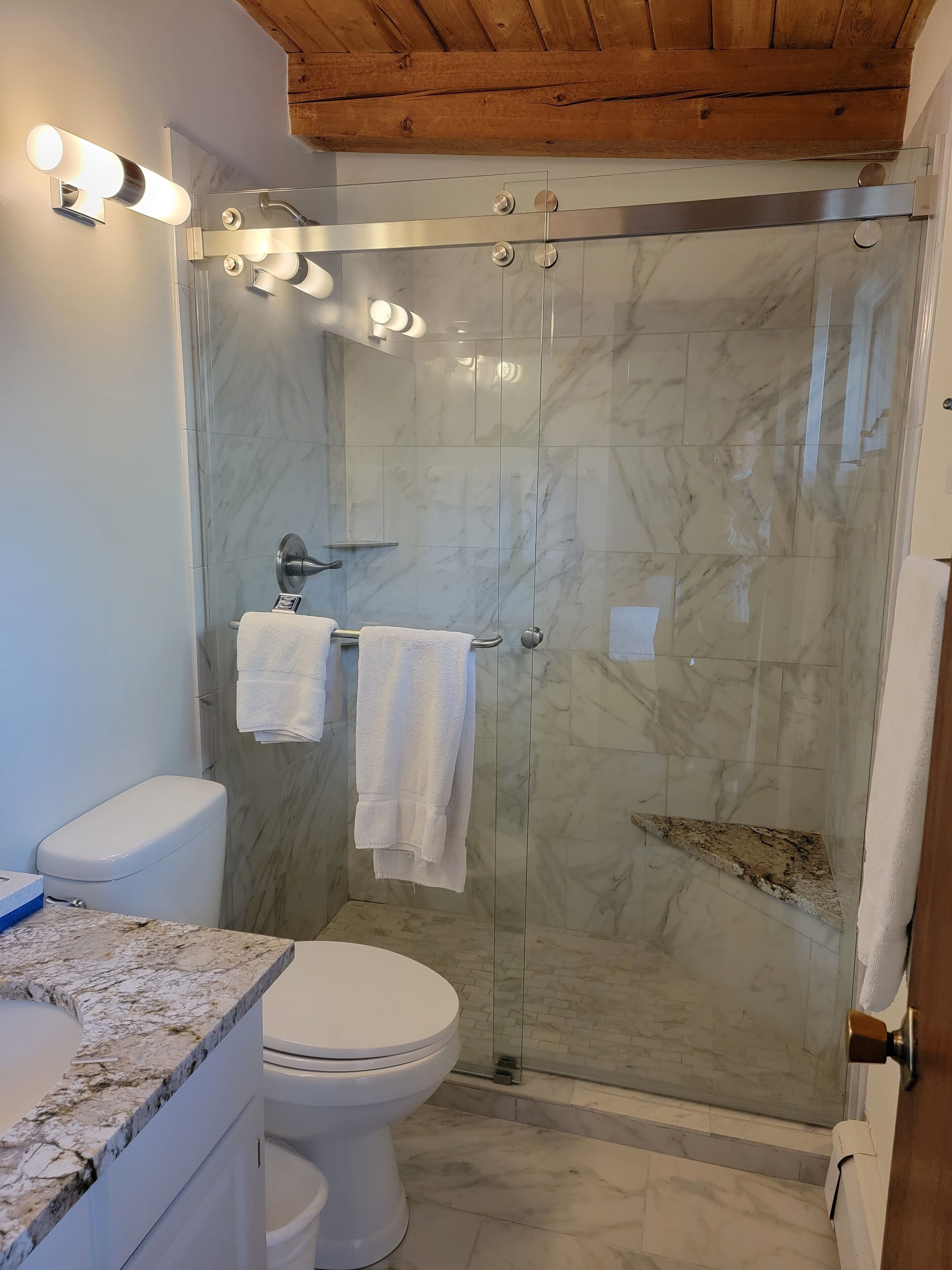 A modern bathroom with a glass-enclosed shower, marble tiles, a white toilet, and a granite countertop.