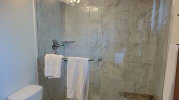 A modern bathroom with a glass-enclosed shower, marble tiles, a white toilet, and a granite countertop.