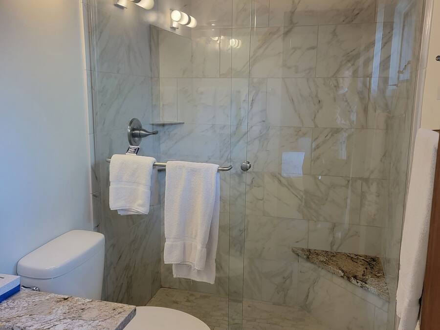 A modern bathroom with a glass-enclosed shower, marble tiles, a white toilet, and a granite countertop.