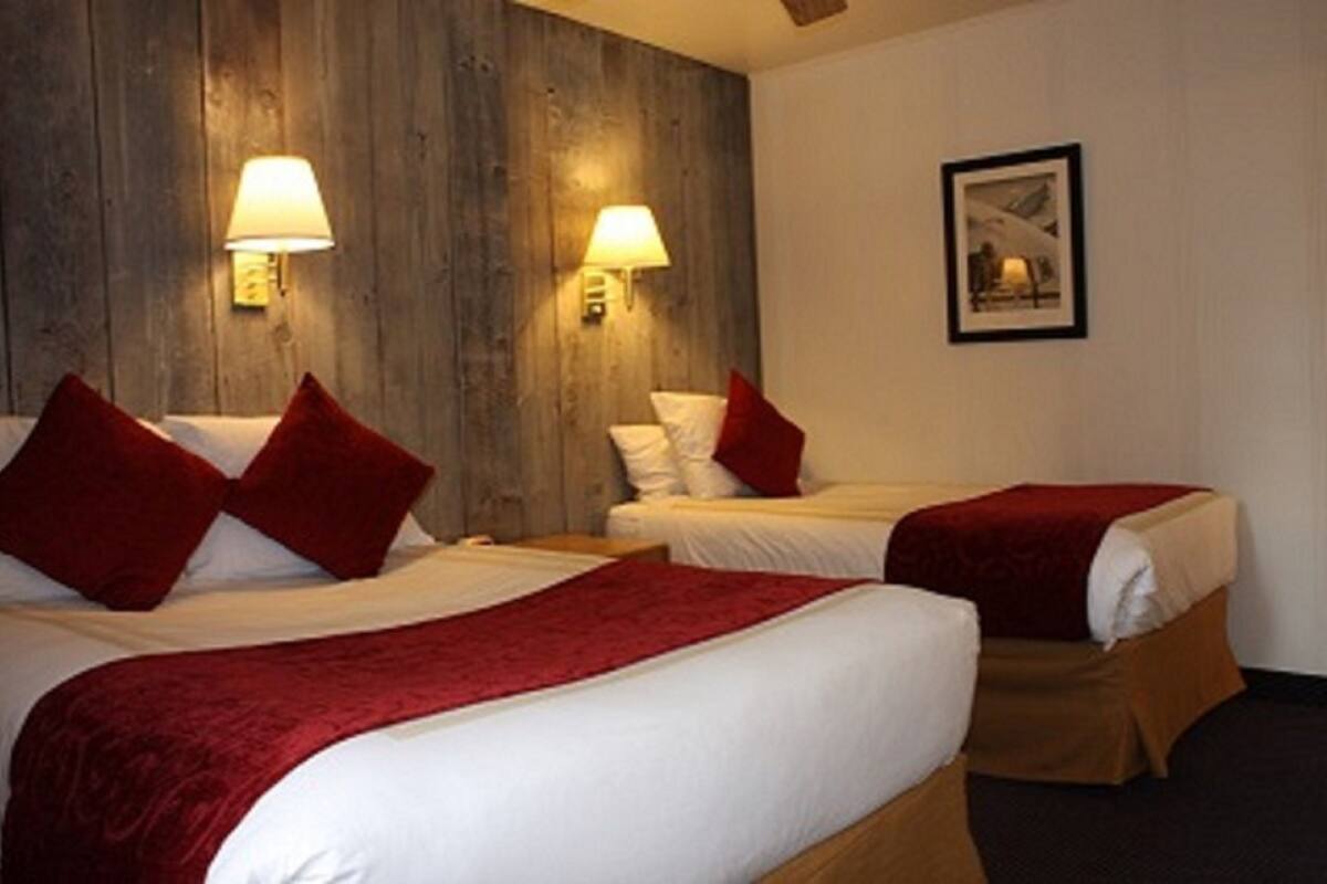 Habitación de hotel con dos camas, cada una con almohadas y manta rojas. Hay lámparas fijadas a la pared a cada lado de las camas.