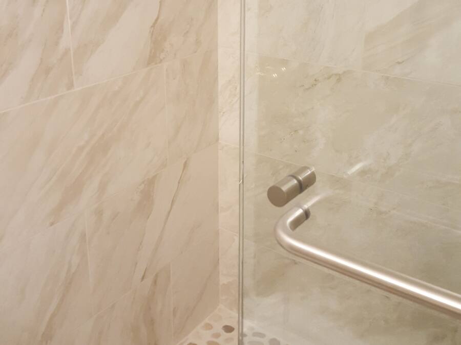 A shower with a glass door, a metal handle, and a handrail.