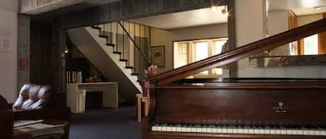 Un piano à queue se trouve dans une pièce spacieuse, et un escalier mène à un niveau supérieur.
