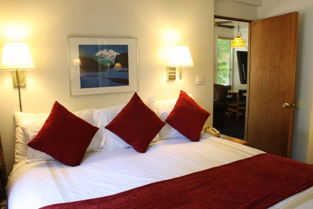 Habitación de hotel con cama, almohadas rojas, dos lámparas de pared y un cuadro en la pared.