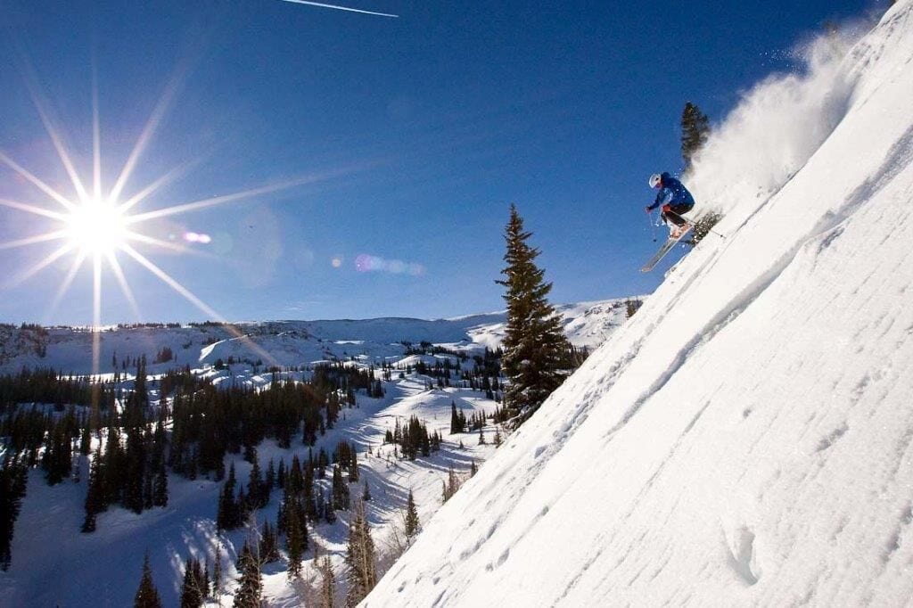 A skier on a snowy slope with a clear sky and sun shining.