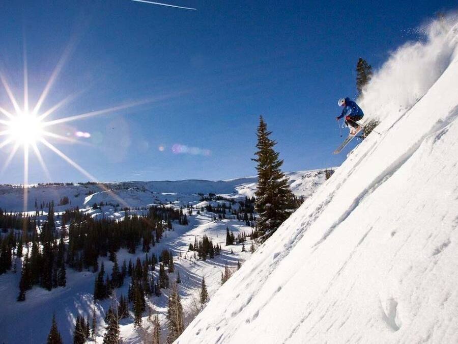 A skier on a snowy slope with a clear sky and sun shining.