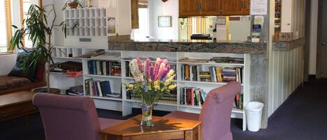 A cozy reading area with a wooden table, two purple chairs, and a bookshelf filled with books and a vase of flowers.