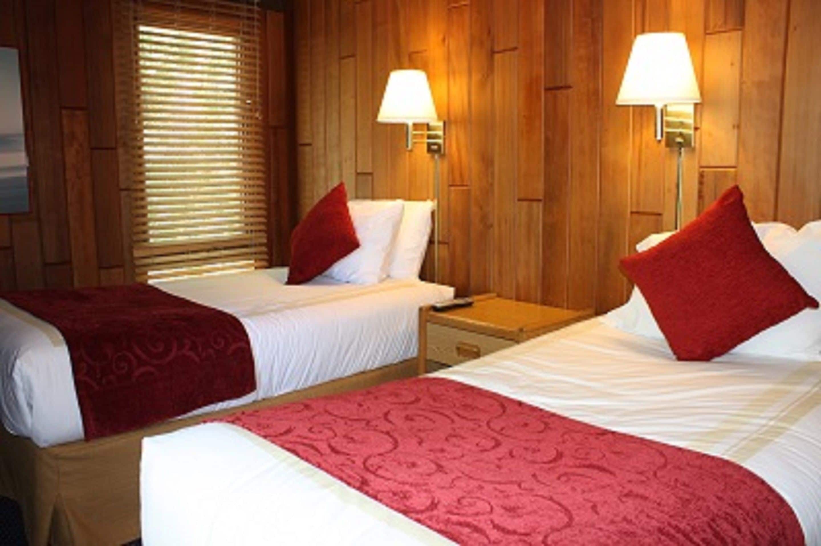 Ett hotellrum med två sängar, träpanel på väggarna och två vägglampor.