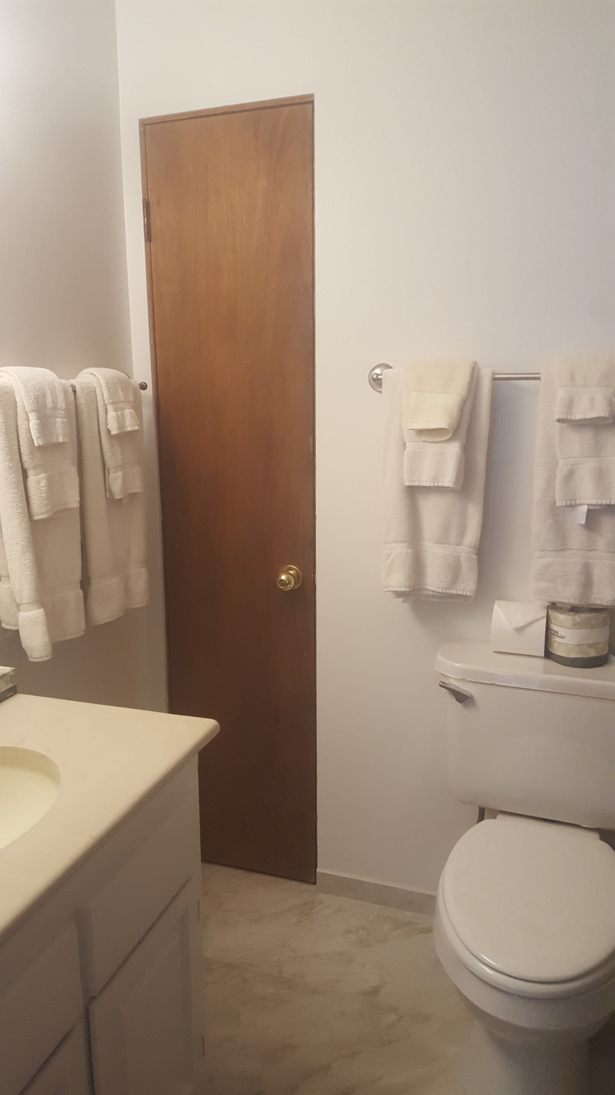 Une salle de bain avec une porte en bois, des toilettes et plusieurs serviettes blanches suspendues à un porte-serviettes.