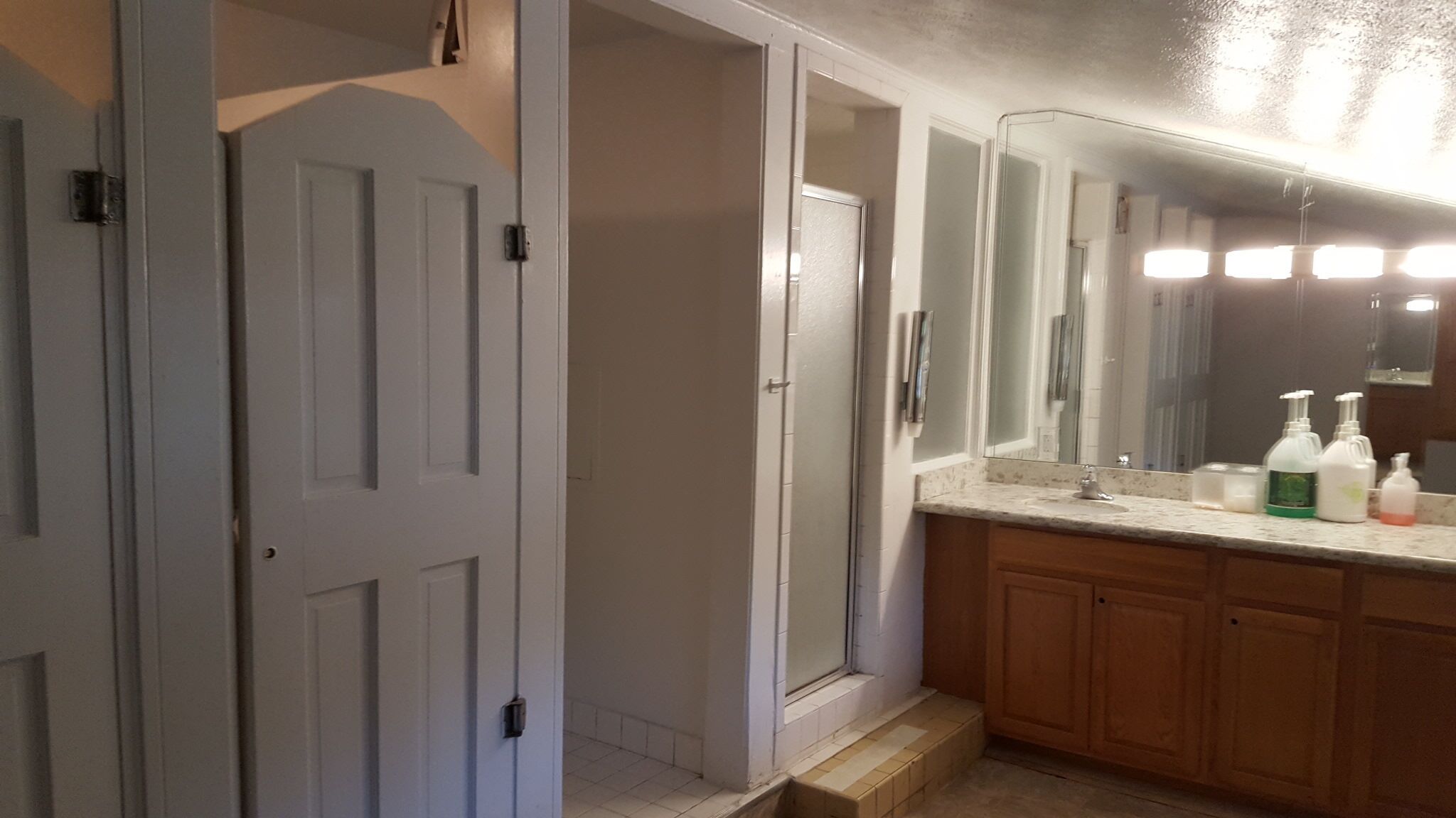A bathroom with a white door, a mirror, and a countertop with toiletries.