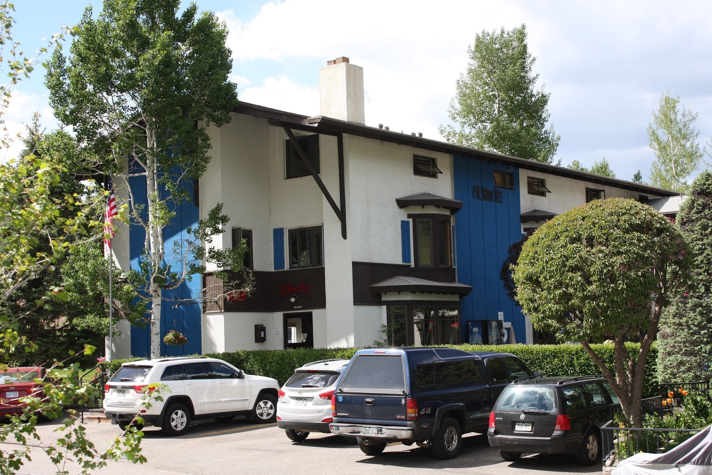 A building with a blue and white facade, multiple parked cars, and a flag.