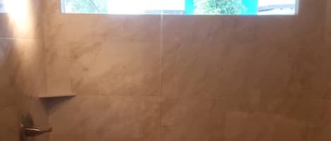 Douchegedeelte met een glazen deur, een handdoekrek en uitzicht op een gebouw door de deur.