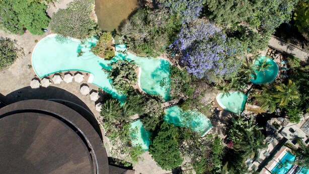 Vista aérea de un complejo turístico con múltiples piscinas rodeado de exuberante vegetación y palmeras.