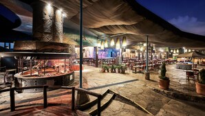 Un espacio exterior para comer con suelo de piedra, plantas en macetas y una parrilla grande en el centro.