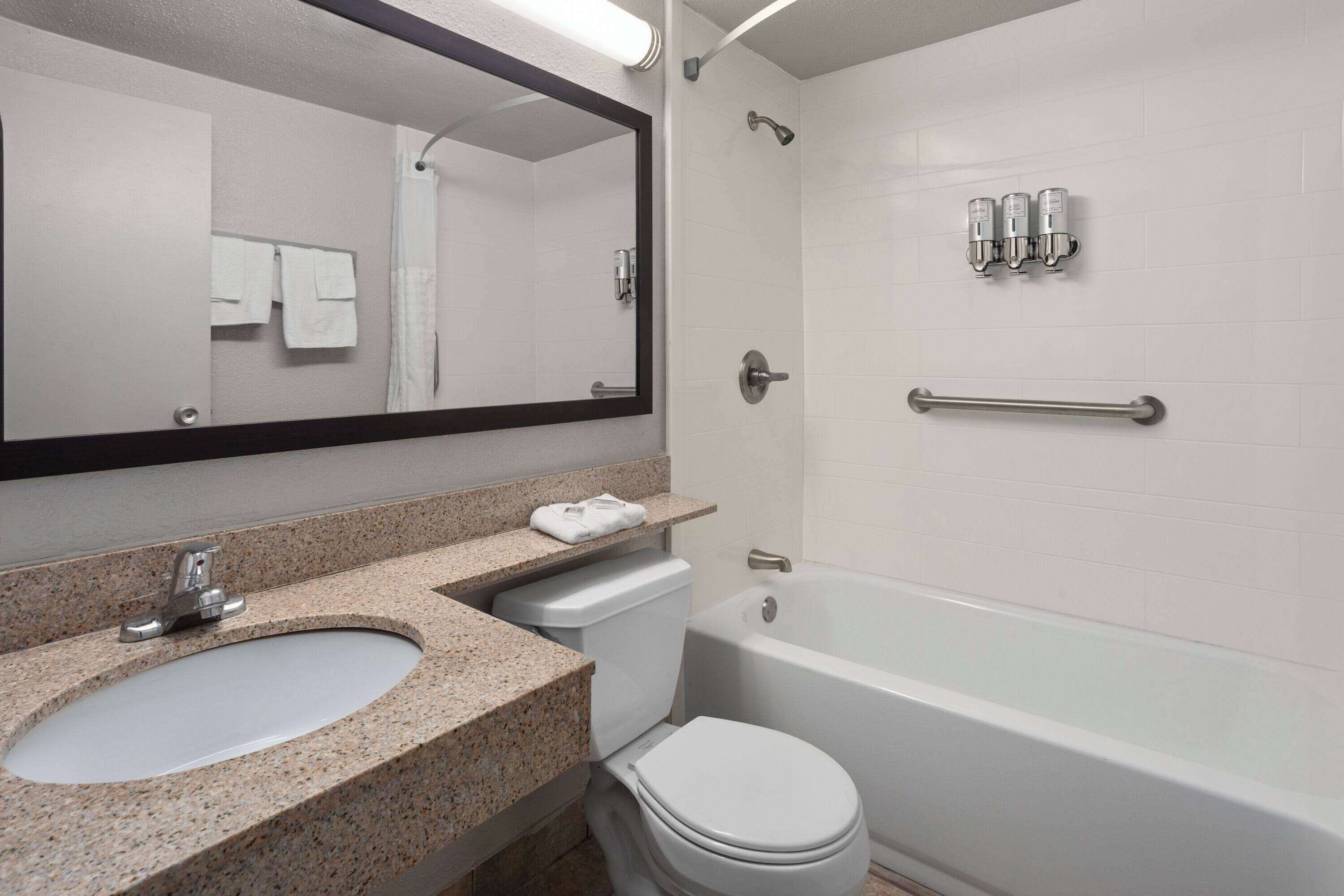 A bathroom with a granite countertop sink, a toilet, a bathtub, a shower, and a mirror.