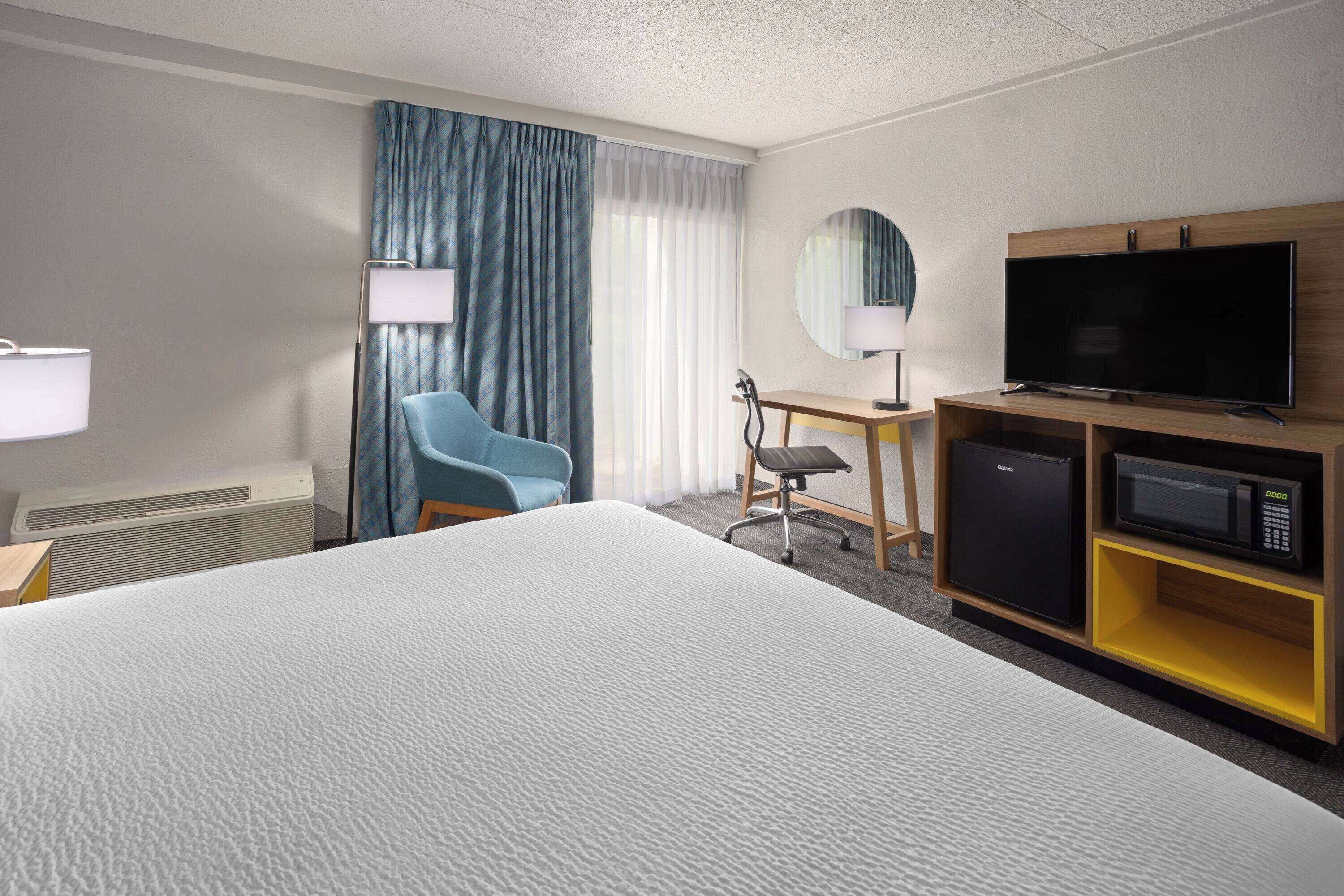 Ein Hotelzimmer mit einem großen Bett, einem Schreibtisch mit Stuhl, einem Fernseher, einer Mikrowelle und einem kleinen Kühlschrank.