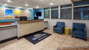 A reception area with a reception desk, a blue armchair, a yellow side table, and a large window with blinds. - Days Inn by Wyndham Ann Arbor (Ann Arbor)