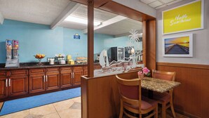 A kitchen with wooden cabinets, a blue wall, a counter with a coffee machine, and a table with chairs. - Days Inn by Wyndham Ann Arbor (Ann Arbor)