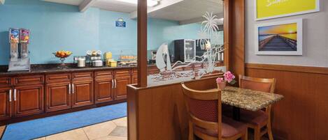 A kitchen with wooden cabinets, a blue wall, a counter with a coffee machine, and a table with chairs.
