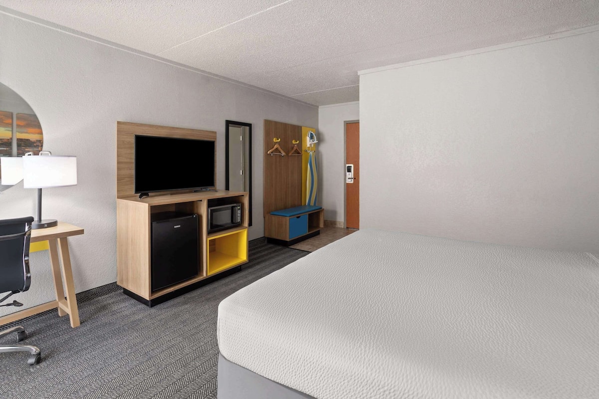 A hotel room with a bed, a desk with a lamp, a TV, a microwave, and a wardrobe.