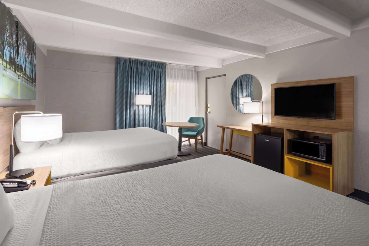A hotel room with two beds, a desk, a TV, and a refrigerator.