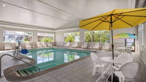 An indoor swimming pool with clear water, surrounded by white chairs and a table with a yellow umbrella. - Days Inn by Wyndham Ann Arbor (Ann Arbor)