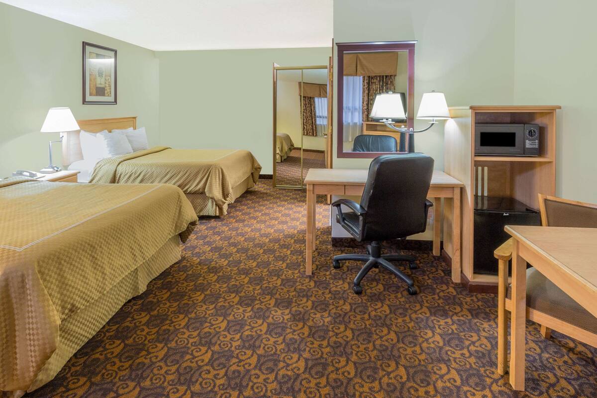 Ein Hotelzimmer mit zwei Betten, einem Schreibtisch, einem Stuhl, einer Mikrowelle und einem Spiegel.