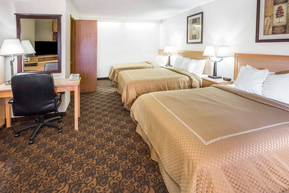 Ein Hotelzimmer mit zwei Einzelbetten, einem Schreibtisch mit Stuhl, einem Fernseher und einem Spiegel.