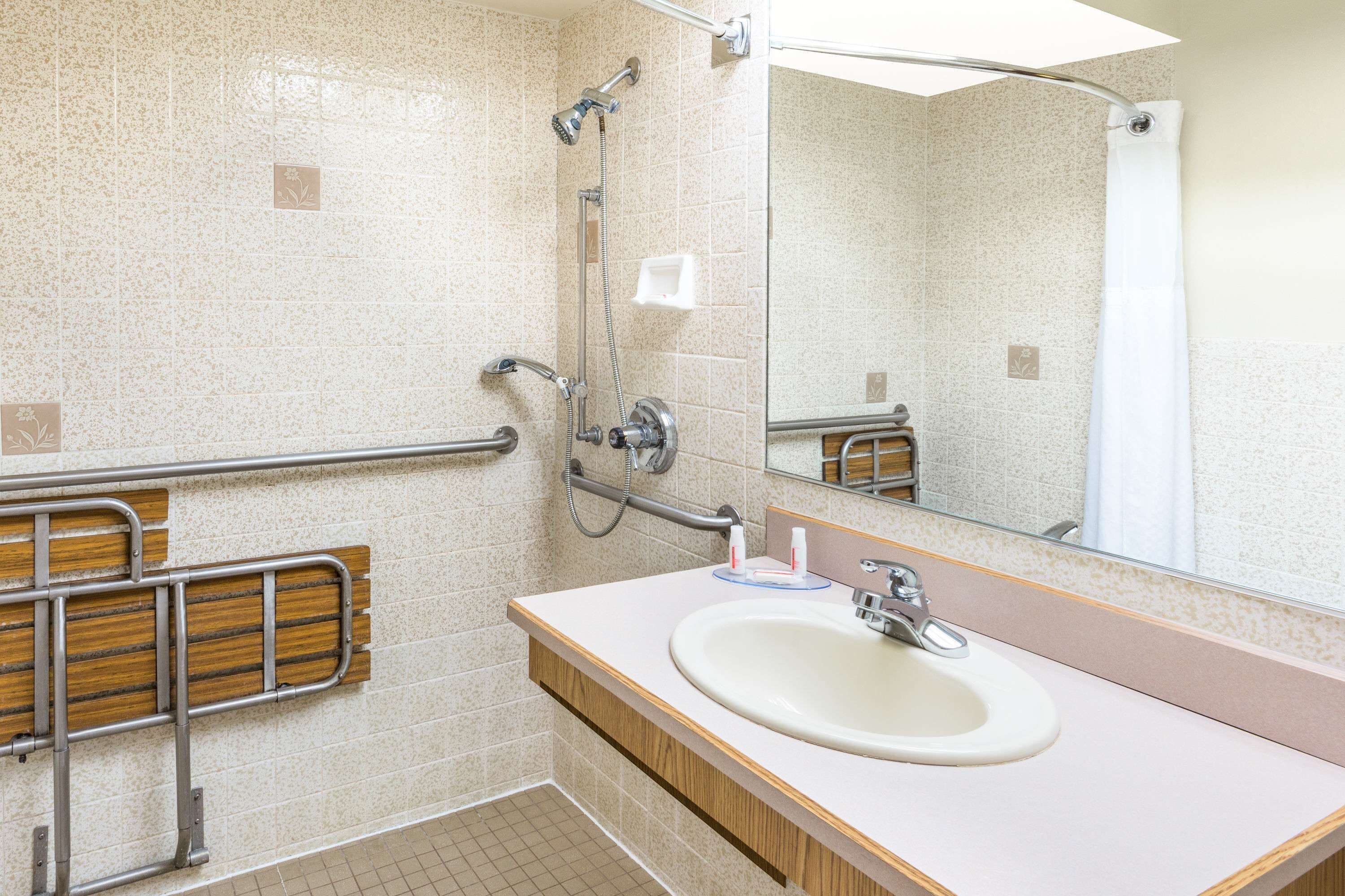 Une salle de bain équipée d’un lavabo, d’un miroir et de barres d’appui.