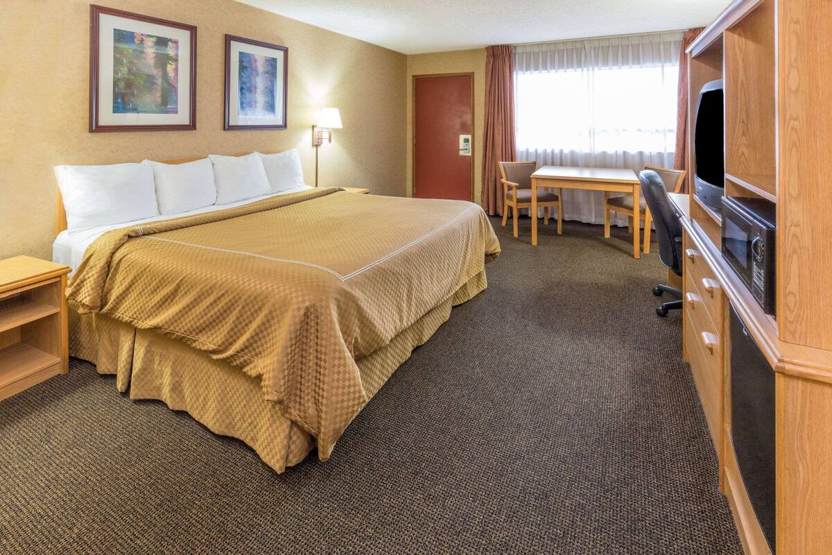 Ein Hotelzimmer mit einem großen Bett, einem Schreibtisch, einem Sessel, einem Fernseher und einem Kleiderschrank.