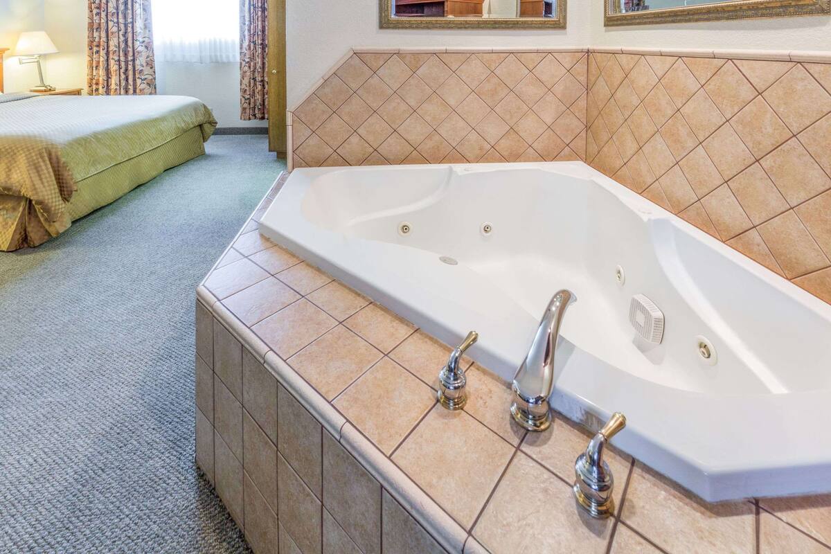 Ein Badezimmer mit einer großen weißen Badewanne, einer hölzernen Sitzbank und einer gefliesten Wand.